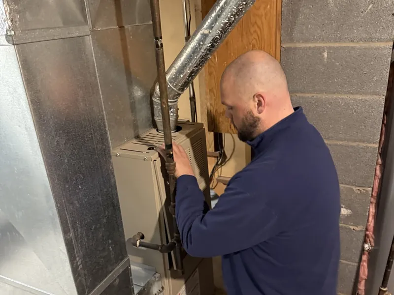 Commodore technician kneeling beside a basement furnace while diagnosing and repairing the gas line