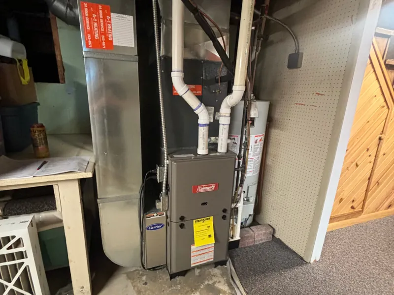 Replacement Coleman high-efficiency gas furnace installed next to ductwork and a water heater in a basement