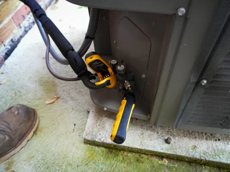 Refrigerant gauge and service tools attached to an outdoor AC unit during a maintenance tune-up